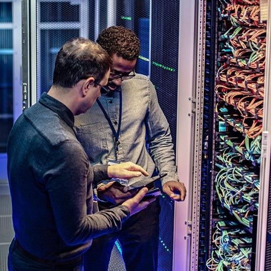 Two men in a server room discussing data protection and looking at a tablet